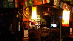 A bar area with a counter, flags, and a person working behind the bar. - Leo Hostel (Beijing)