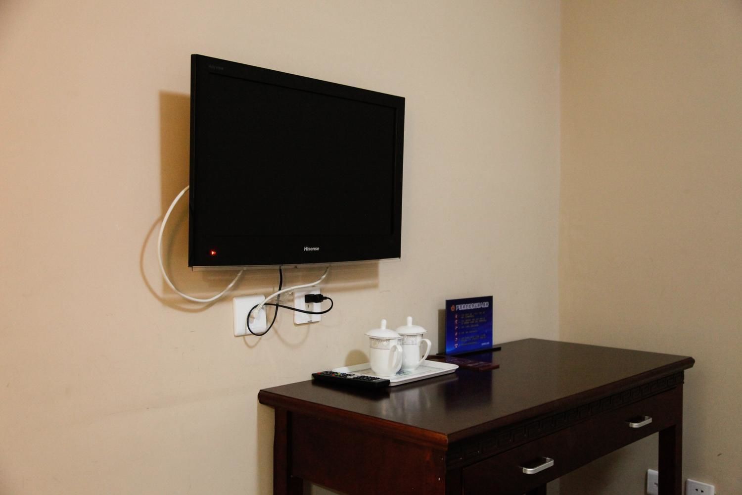 A television mounted on a wall, a wooden desk with a remote control, and a sign with text.