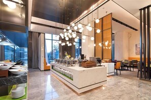 A modern hotel lobby with a central breakfast bar, large windows, and contemporary lighting fixtures. - Hampton Hilton Beijing Conference Center (BEIJING)