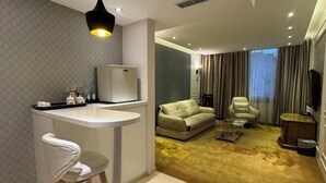 A modern living room with a sofa, armchair, and coffee table, a small kitchen area with a refrigerator, and a dining area with a bar stool. - Lotus Hotel (Kunming)