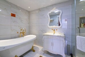 Un baño con una bañera independiente, un tocador con espejo y baldosas de mármol.