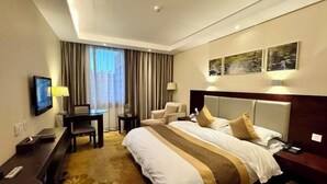 A hotel room with a large bed, a desk, a chair, a TV, and artwork on the wall. - Lotus Hotel (Kunming)