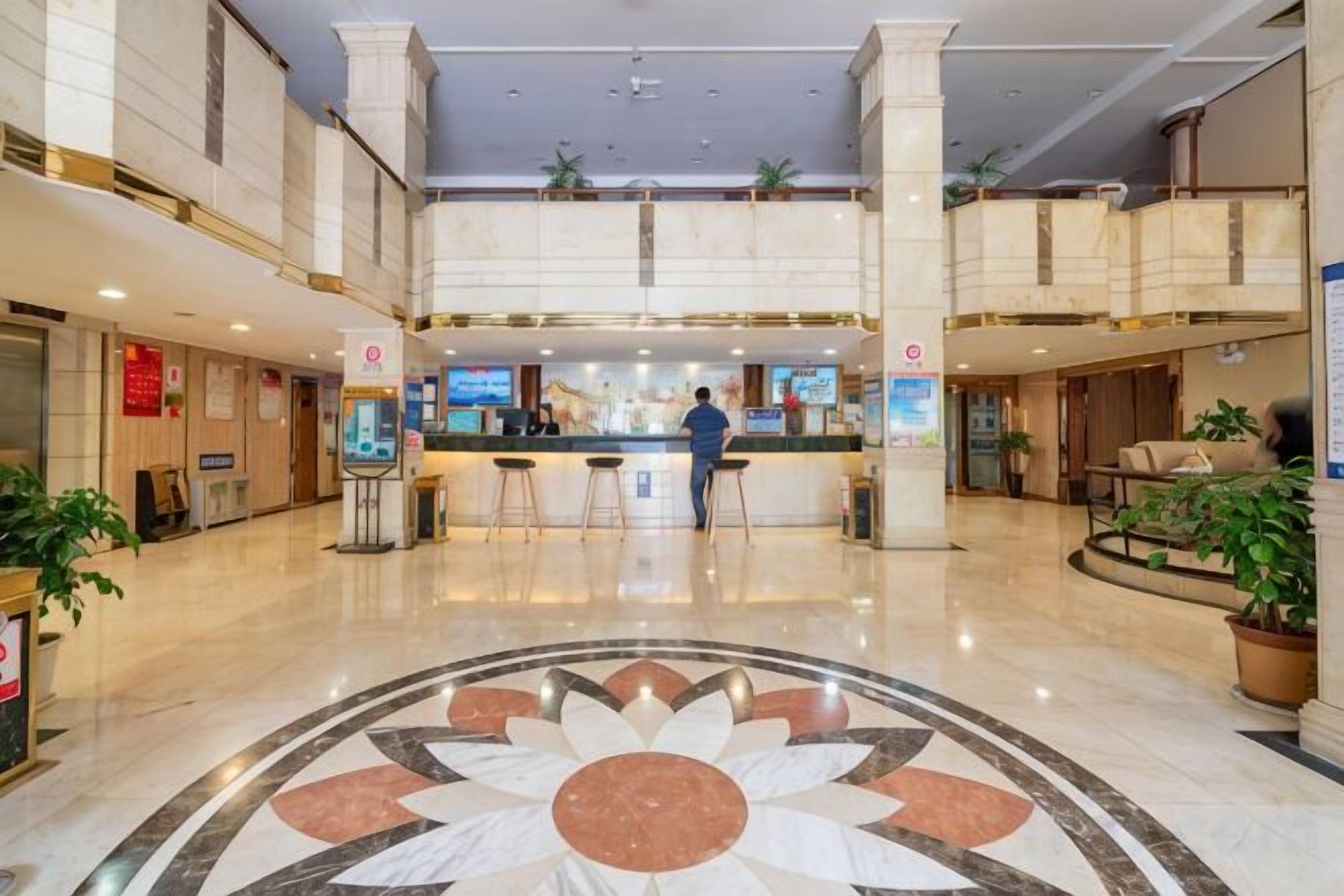 A hotel lobby with a central reception desk, seating area, and a decorative floor pattern.