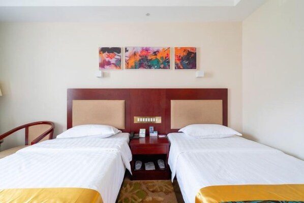A hotel room with two beds, a wooden headboard, a nightstand, and a pair of wall-mounted artwork.