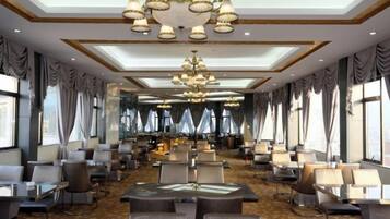 A spacious hotel lobby with multiple seating areas, a central chandelier, and large windows allowing natural light.