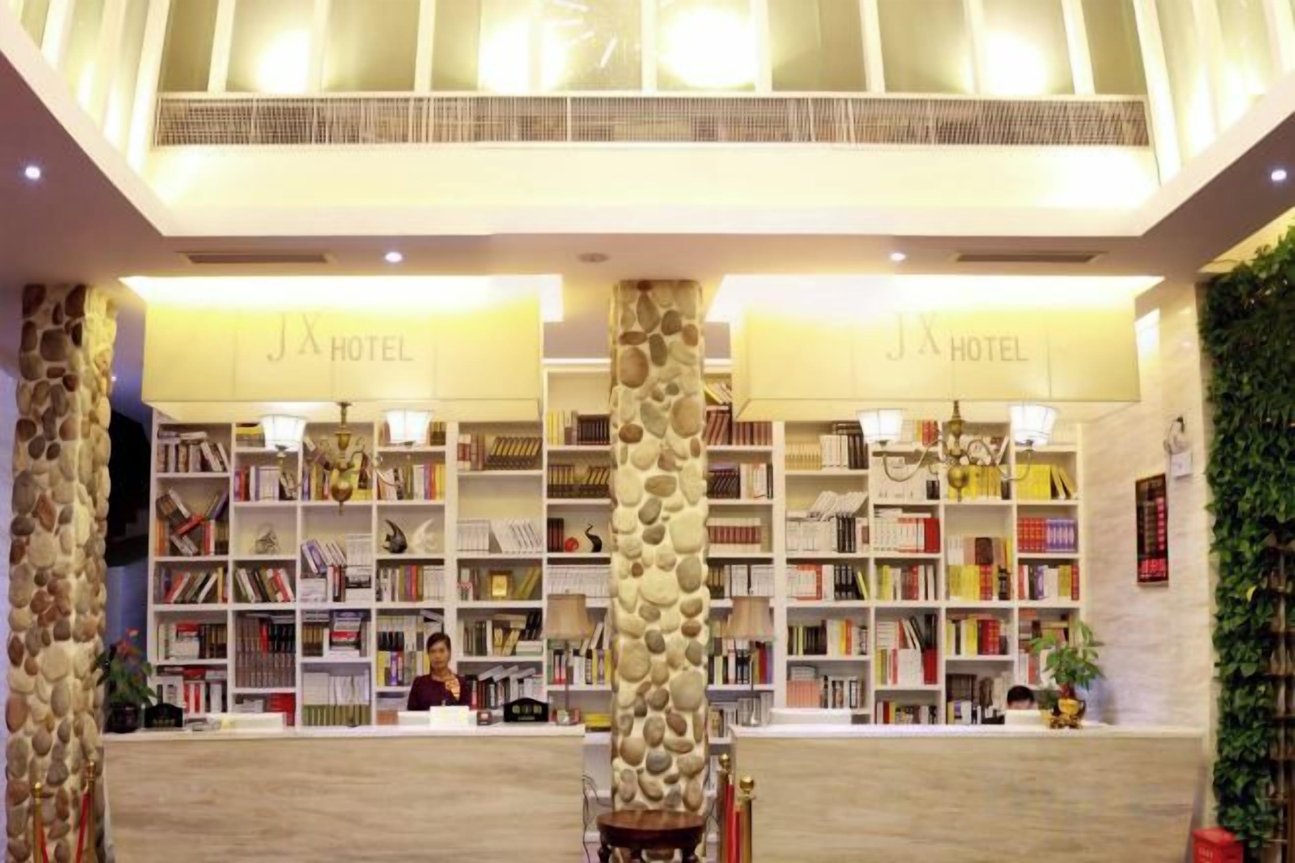 A hotel lobby with a reception desk, bookshelves, and a chandelier.