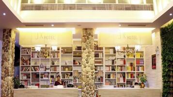 A hotel lobby with a reception desk, bookshelves, and a chandelier.