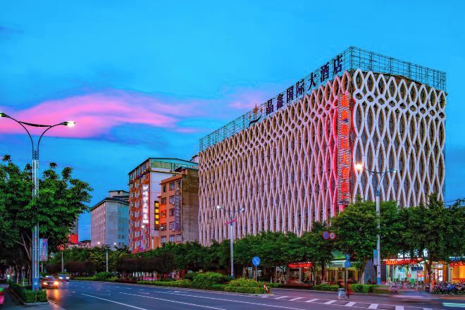 A modern building with a unique facade, surrounded by trees and a street.