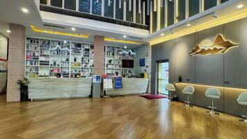 A hotel lobby with a reception desk, bookshelves, and a seating area.