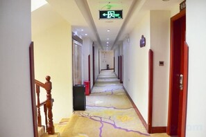 Un couloir d'hôtel avec un sol recouvert de moquette, des portes en bois et un escalier.