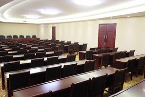 Une salle de conférence avec des rangées de tables et de chaises, une grande porte rouge et un sol recouvert de moquette.