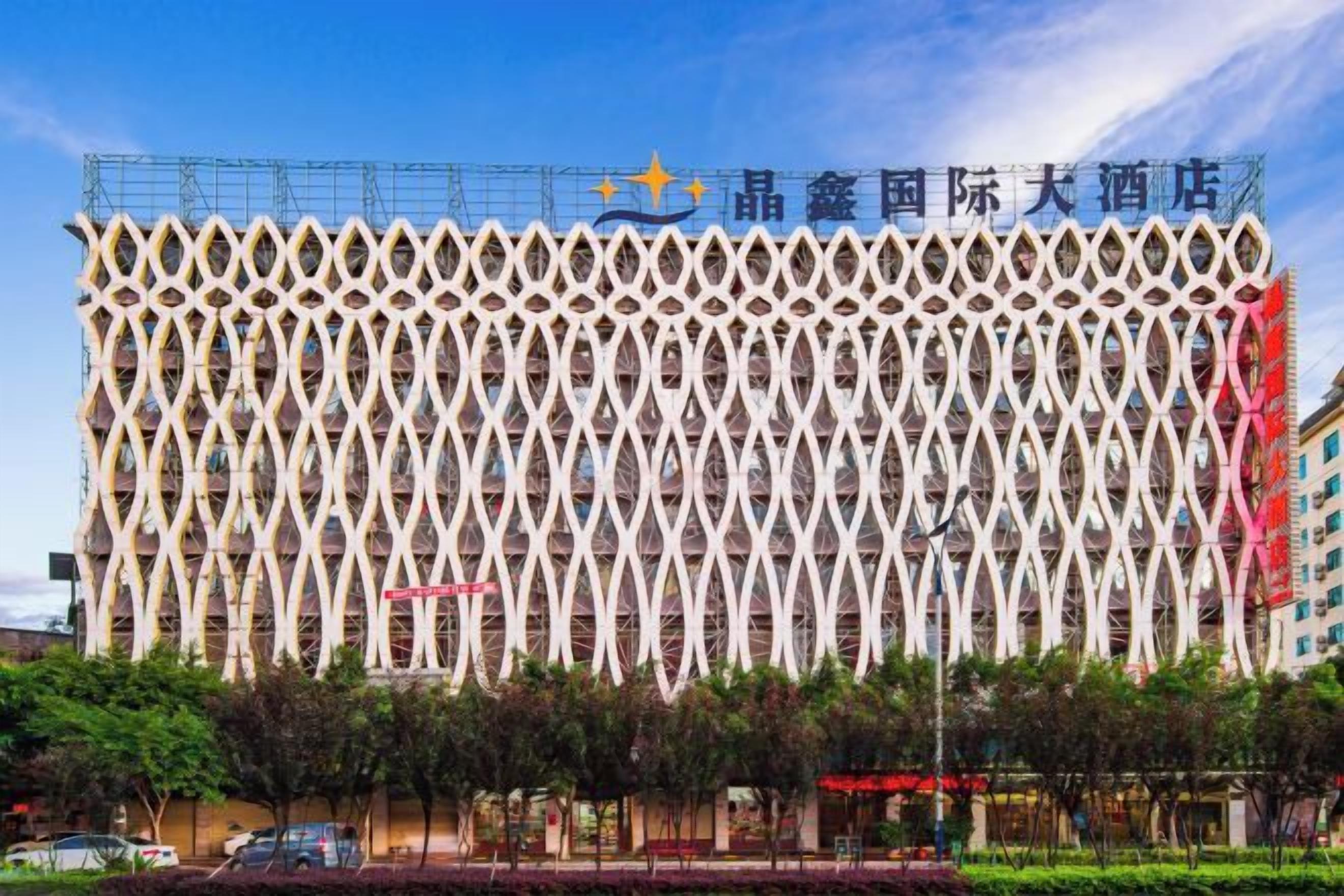 A building with a distinctive geometric facade, likely a hotel, with a clear sky and some trees in the foreground.