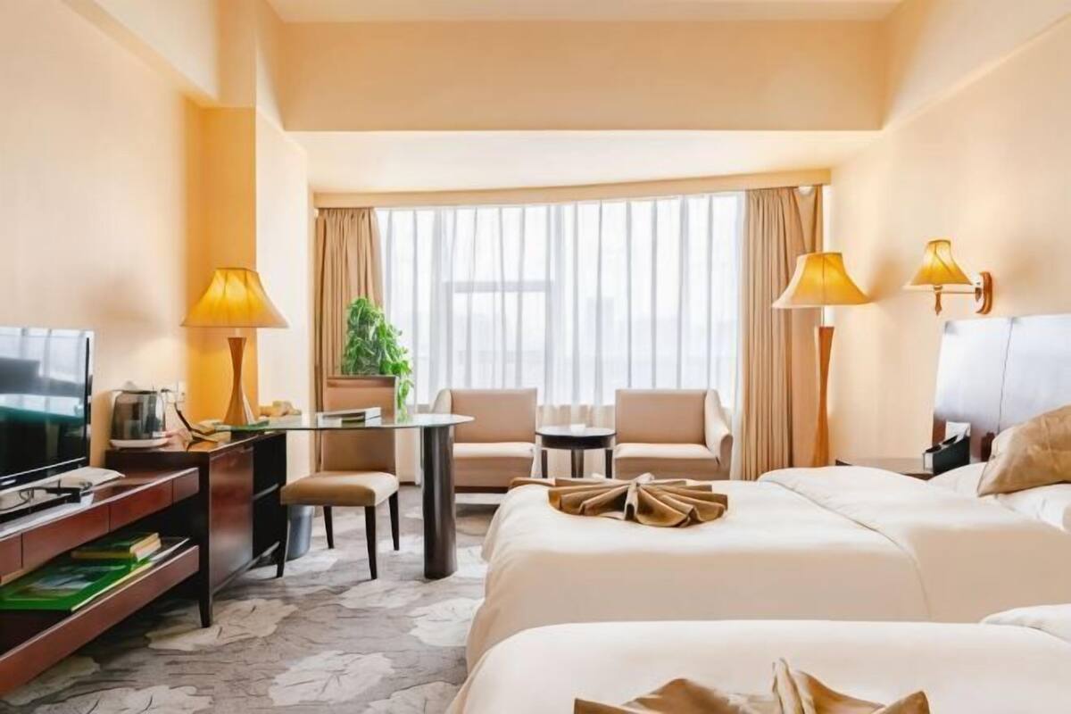 Habitación de hotel con cama, escritorio con lámpara, una silla, televisor y ventana con cortinas.