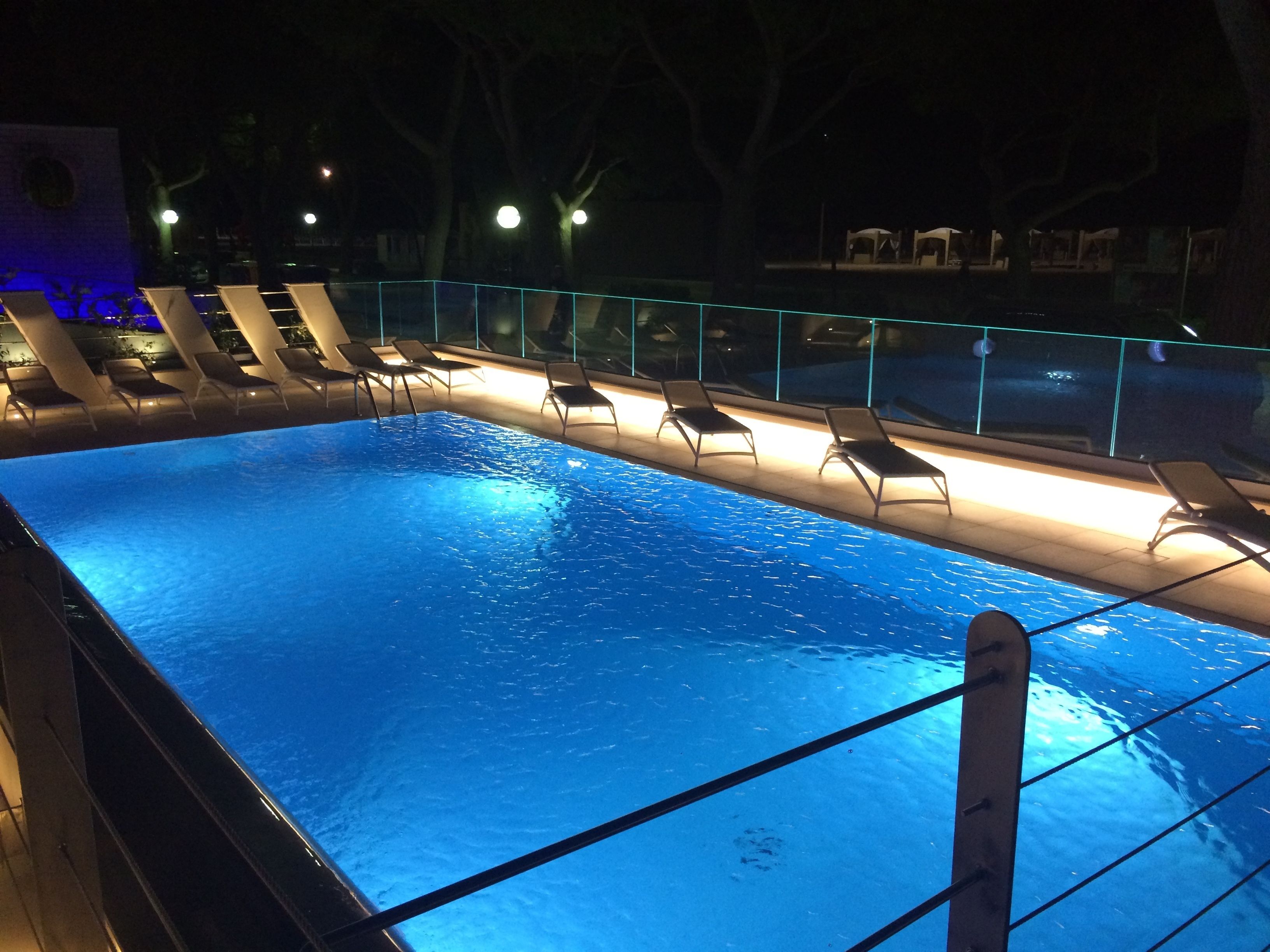 Une piscine intérieure dotée d’une paroi en verre, de chaises longues et d’un éclairage adapté à la nuit.
