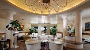 Eine luxuriöse Lobby mit weißen Sofas, einem zentralen Couchtisch und einer großen Kristallleuchtre.'