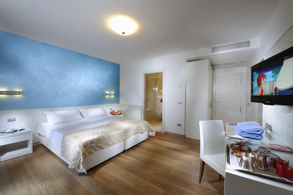 Une chambre d’hôtel moderne dotée d’un grand lit, d’un bureau avec un téléviseur à écran plat et d’une salle de bain visible à travers une porte ouverte.