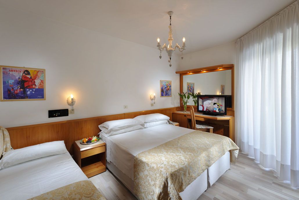 Una camera d'albergo con un letto grande, un comodino con una lampada, una televisione e uno specchio.
