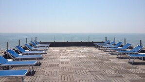 Eine Holzterrasse mit blauen Lounge-Stühlen, die zum Meer hin ausgerichtet sind.
