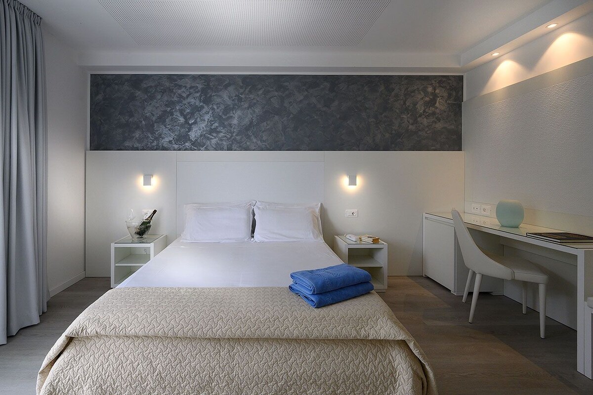 Une chambre d’hôtel moderne, dotée d’un grand lit, de tables de chevet, d’un bureau et d’une chaise.