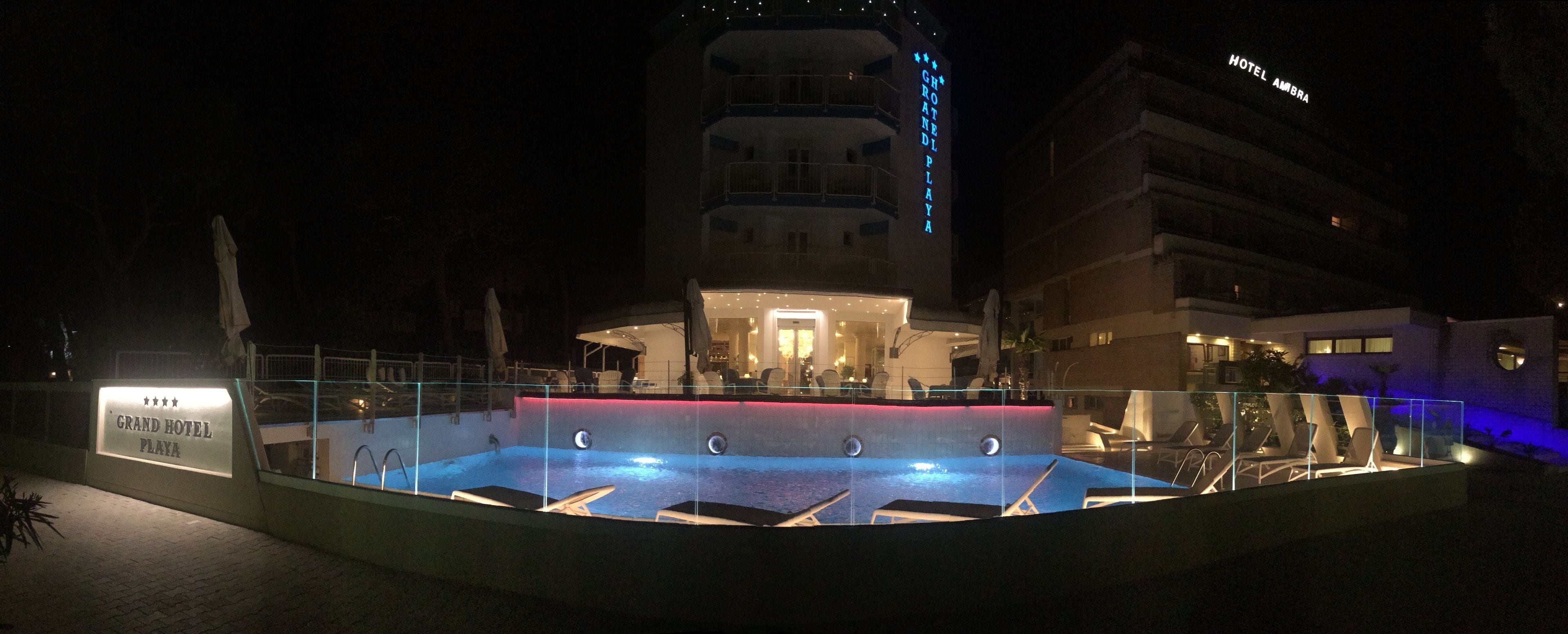 Ein Nachtblick auf das Grand Hotel Playa mit Poolbereich, Bar und einem Gebäude mit Balkonen.