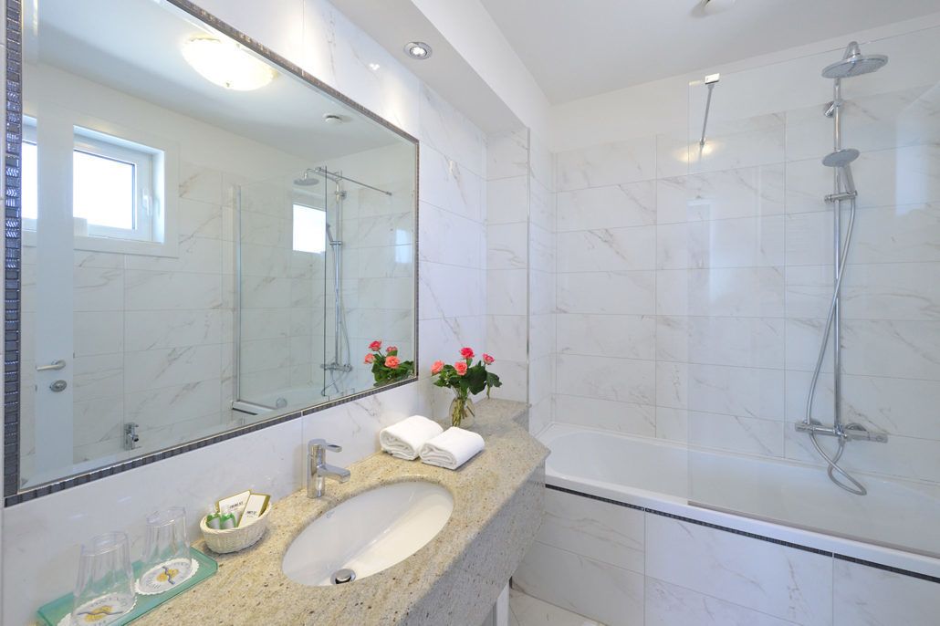 Ein modernes Badezimmer mit Marmorwaschbecken, einem großen Spiegel und einer Dusche mit Glastrennwand.