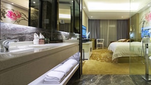 Un baño de hotel moderno con un lavabo de mármol, un banco con toallas, un espejo grande y una televisión.