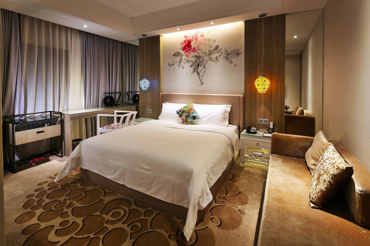 Habitación de hotel con una cama grande, un escritorio, una silla, un sofá y una pared decorativa con una pintura floral.