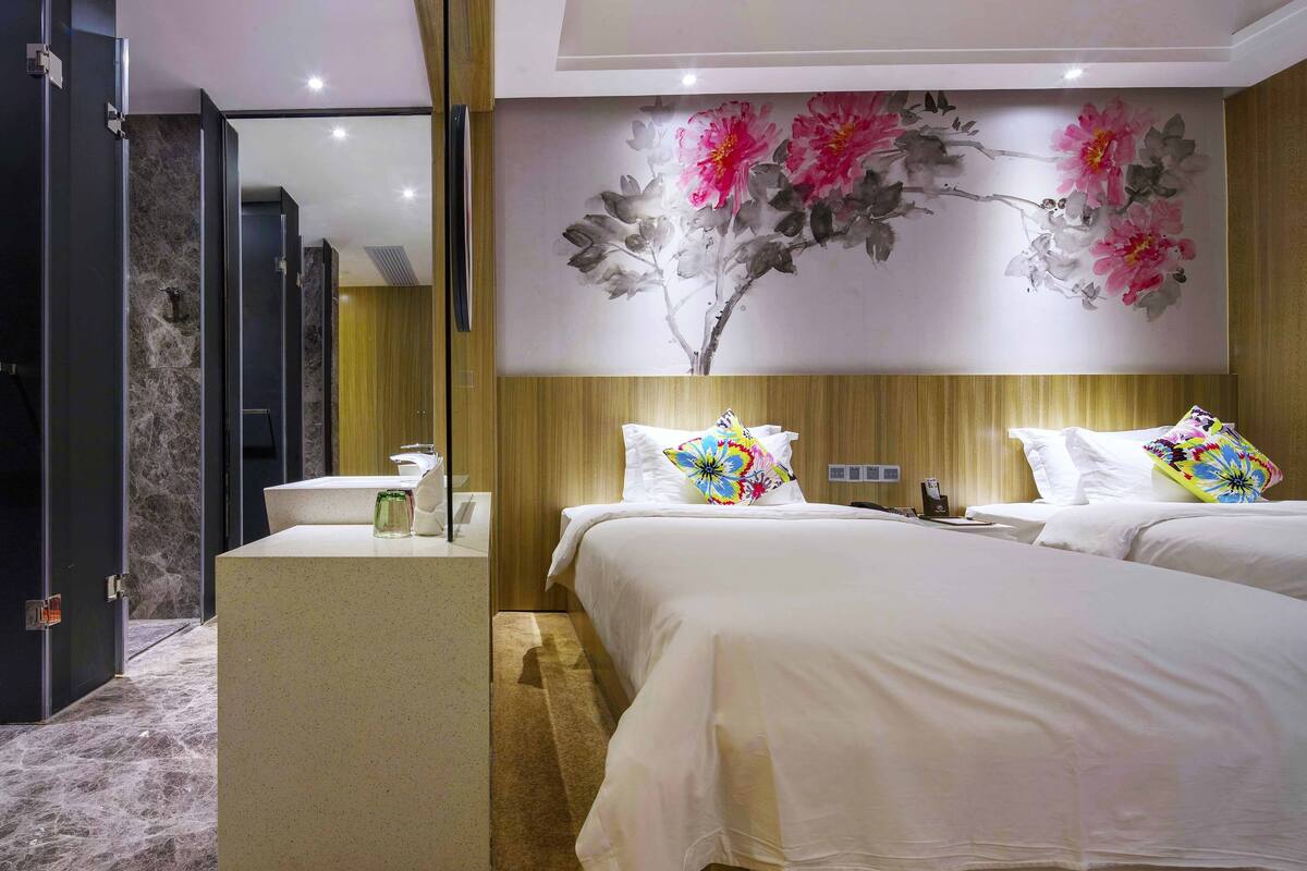 Habitación de hotel con cama, mesita de noche, espejo y un mural floral en la pared.