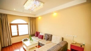 A living room with a sofa, a coffee table, a small table with a plant, a window with curtains, and a red side table with a phone and a basket. - GreenTree Inn Nantong Haimen Bus Statian Shell  Hotel (Nantong)