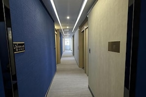 Corredor de hotel com paredes azuis, piso coberto de carpete e portas com números de quarto.