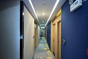 Pasillo de hotel con pisos alfombrados, puertas y un accesorio de iluminación en el techo.