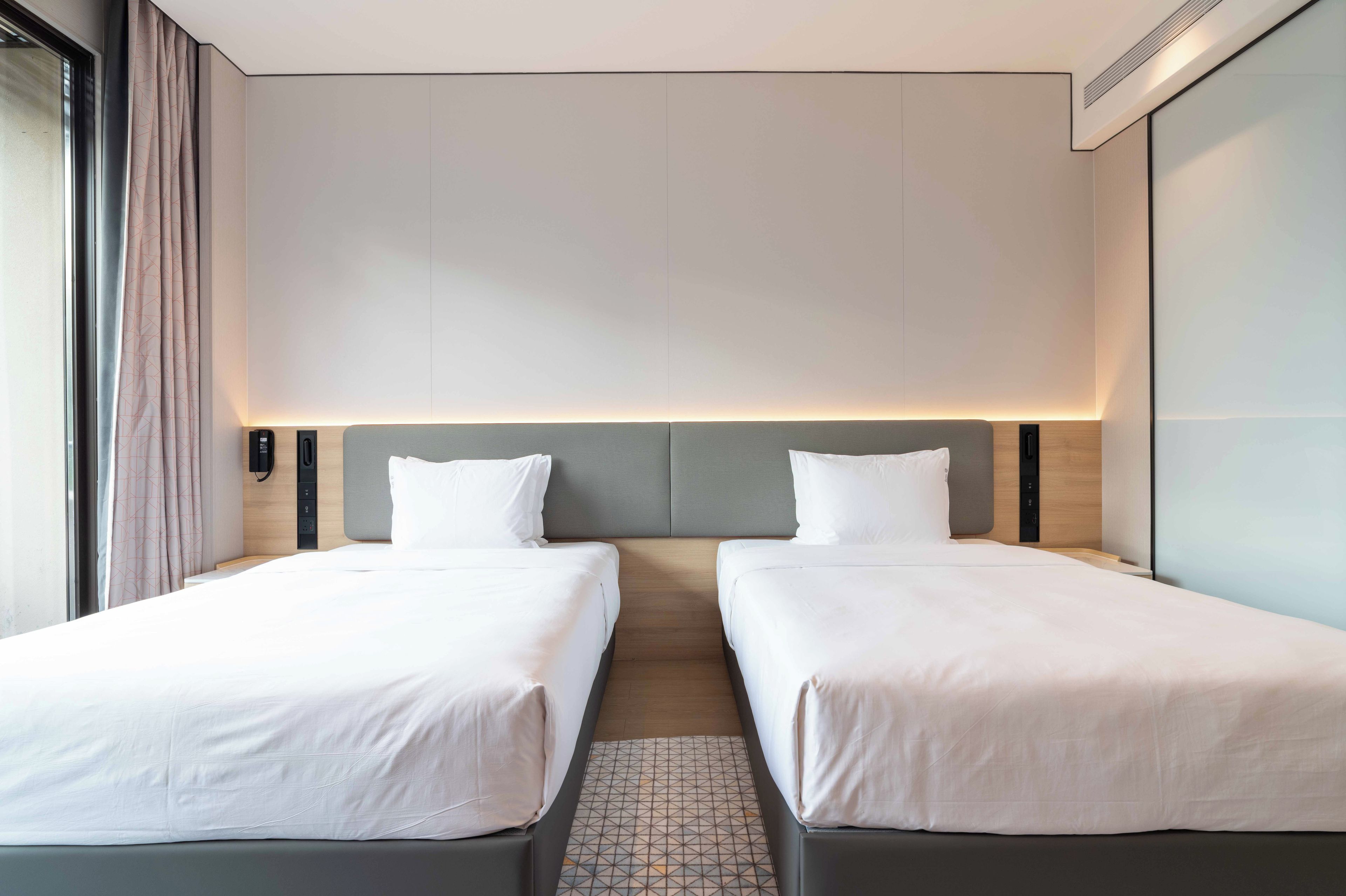 A hotel room with two single beds, a neutral color scheme, and a modern design.