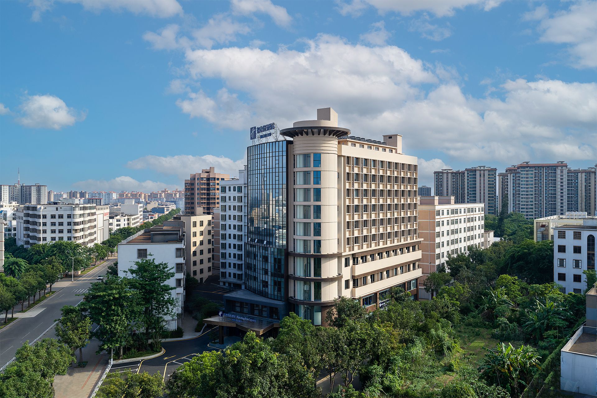 Un hotel de varios pisos con diseño moderno, rodeado de vegetación y otros edificios.