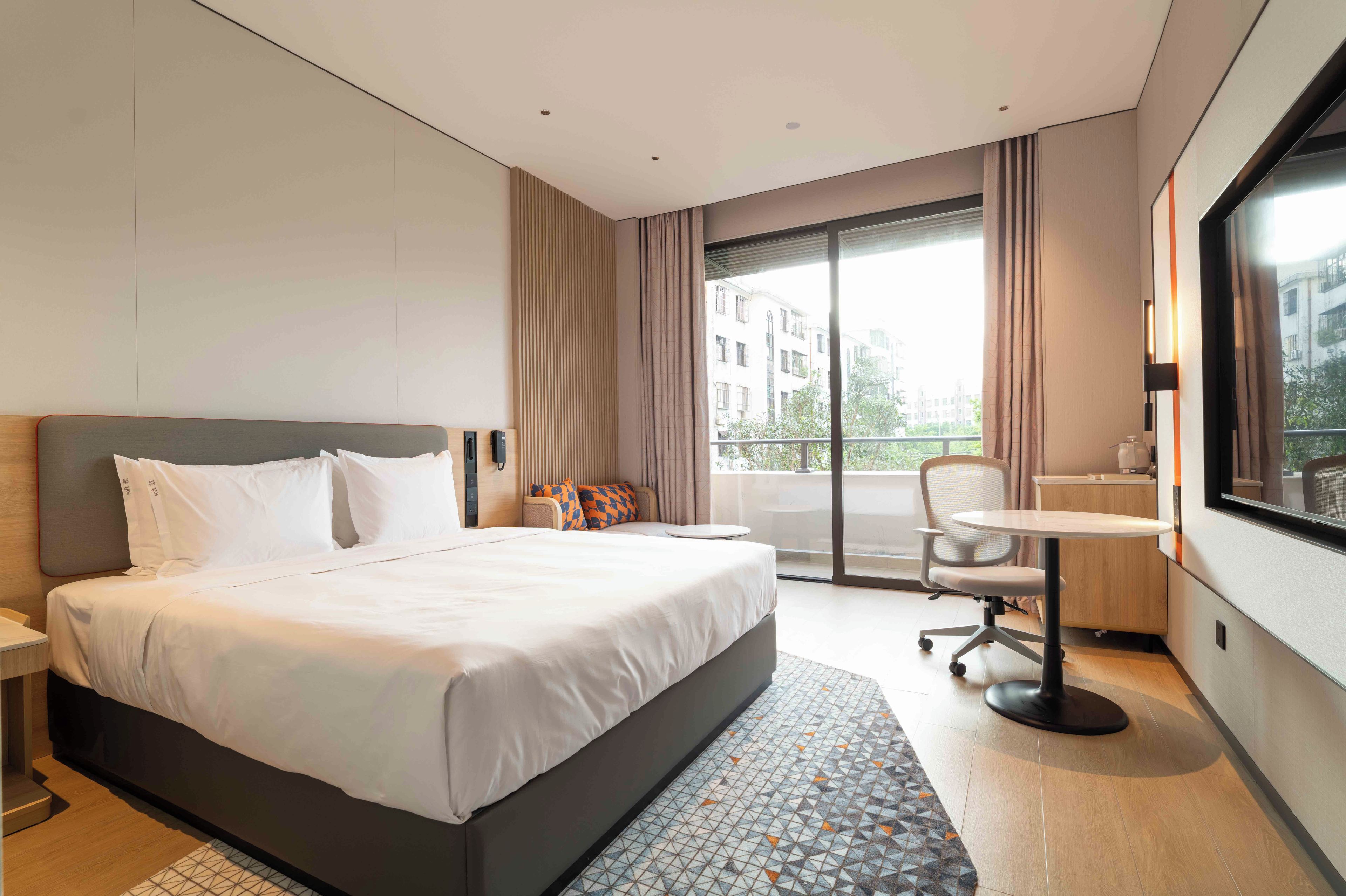 A hotel room with a large bed, a desk, and a view of buildings through the window.