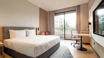 A hotel room with a large bed, a desk, and a view of buildings through the window.