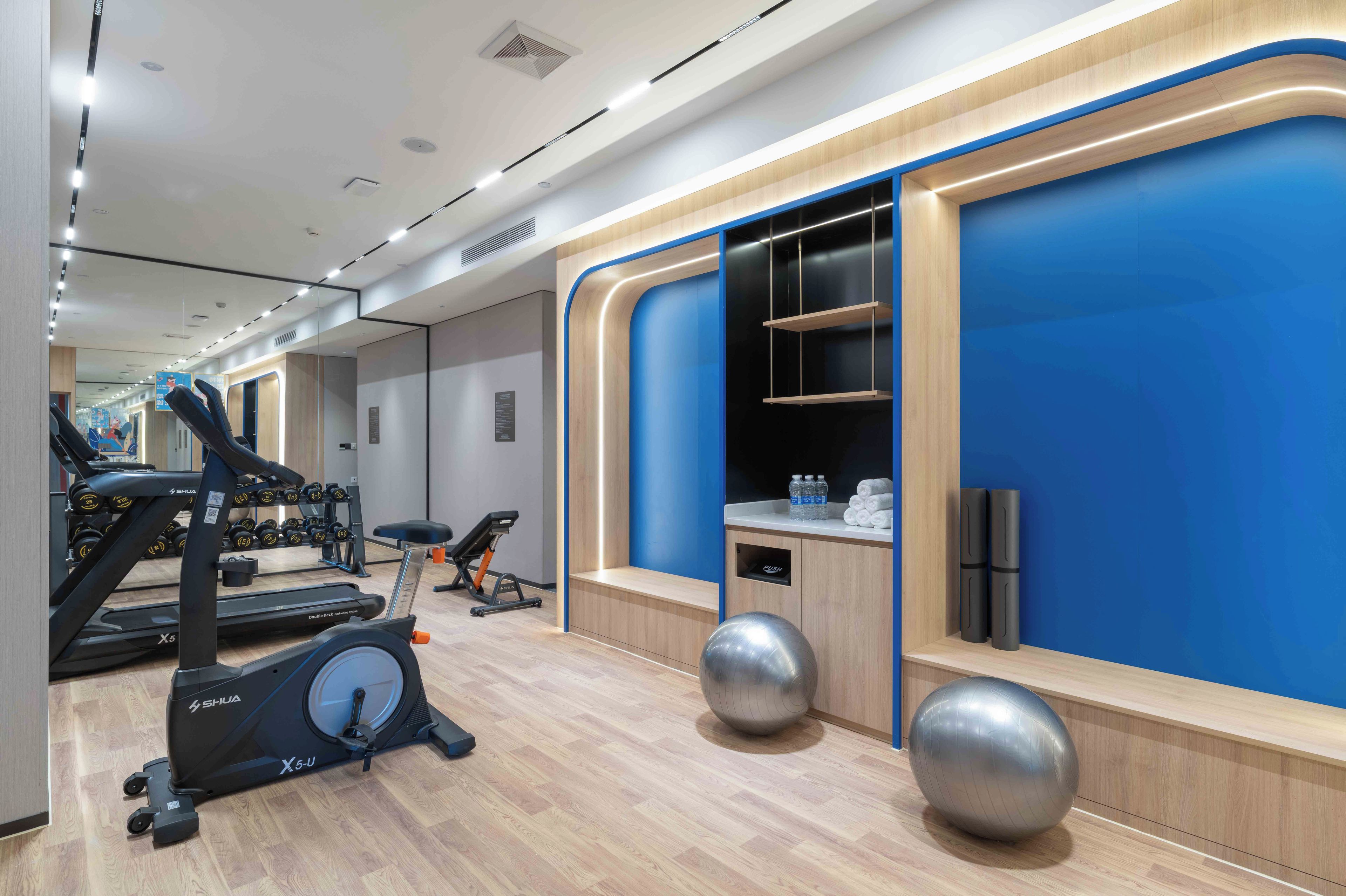 Une salle de sport moderne équipée de matériel d’exercice, avec un mur d’accent bleu et un plancher en bois.