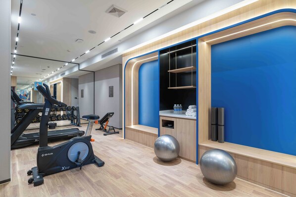 Een moderne sportschool met trainingsapparatuur, een blauwe accentmuur en een houten vloer.