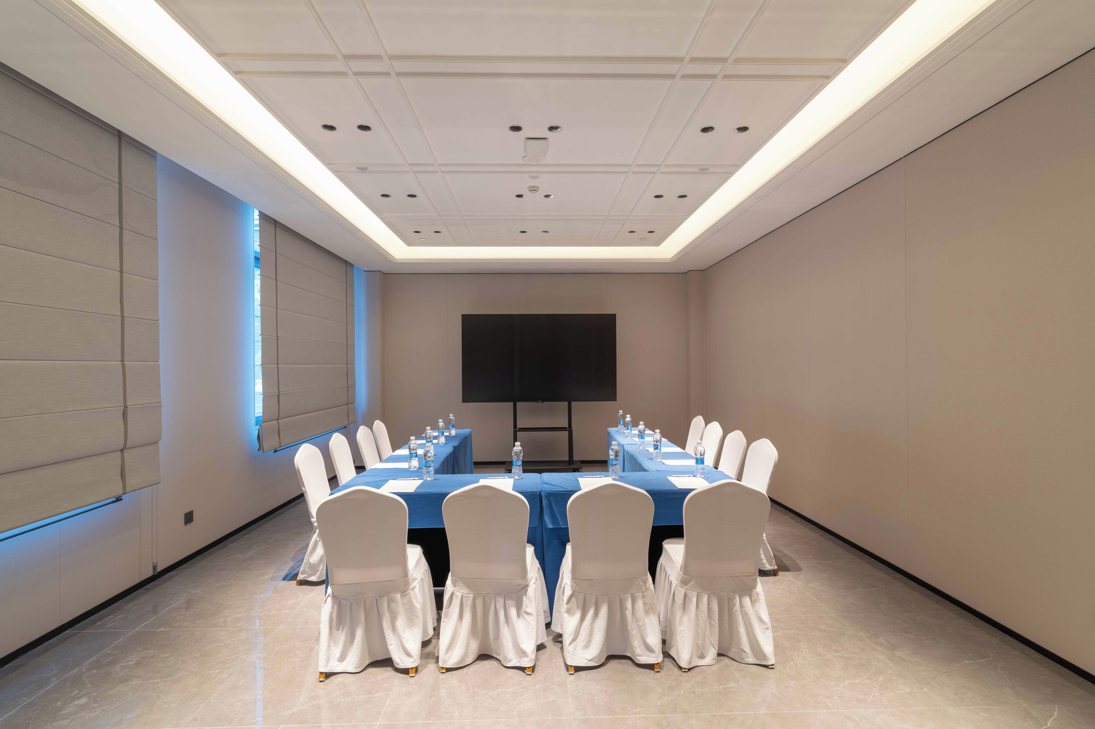 A conference room with a long table, chairs, a projector screen, and a water dispenser.