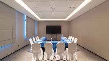 A conference room with a long table, chairs, a projector screen, and a water dispenser.