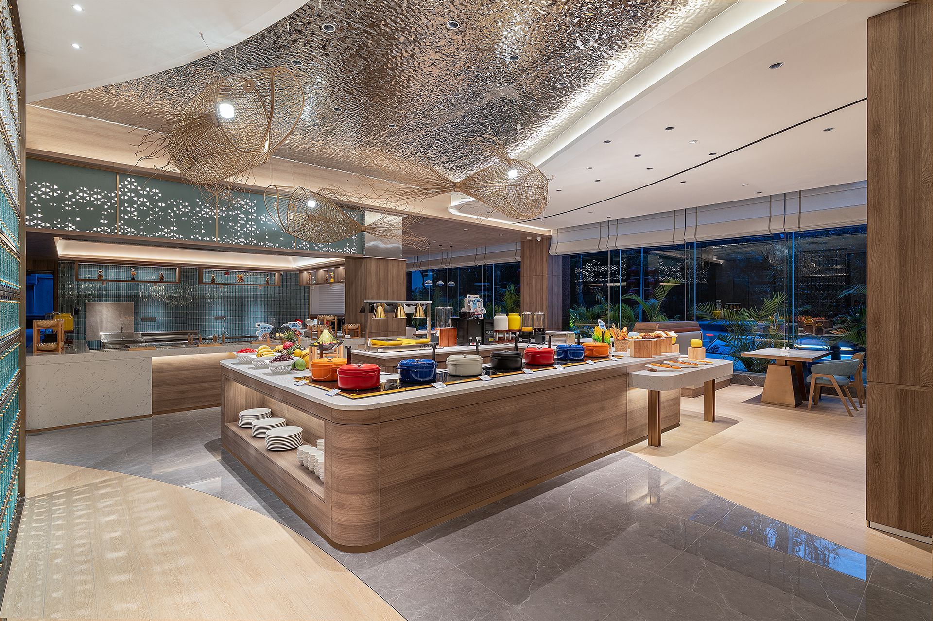 Een moderne keuken met een centraal eiland, een eethoek met een tafel en stoelen, en uitzicht op het buitengebied door grote ramen.