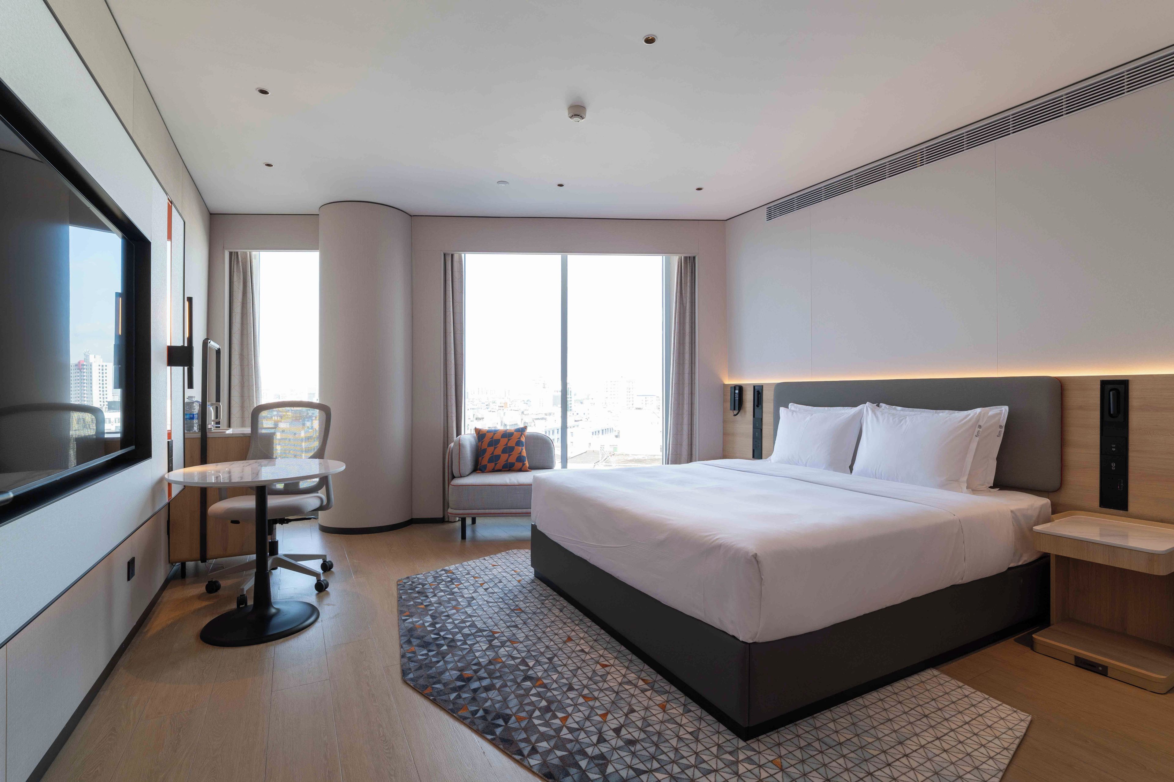 A hotel room with a bed, a desk, a chair, and a large window.