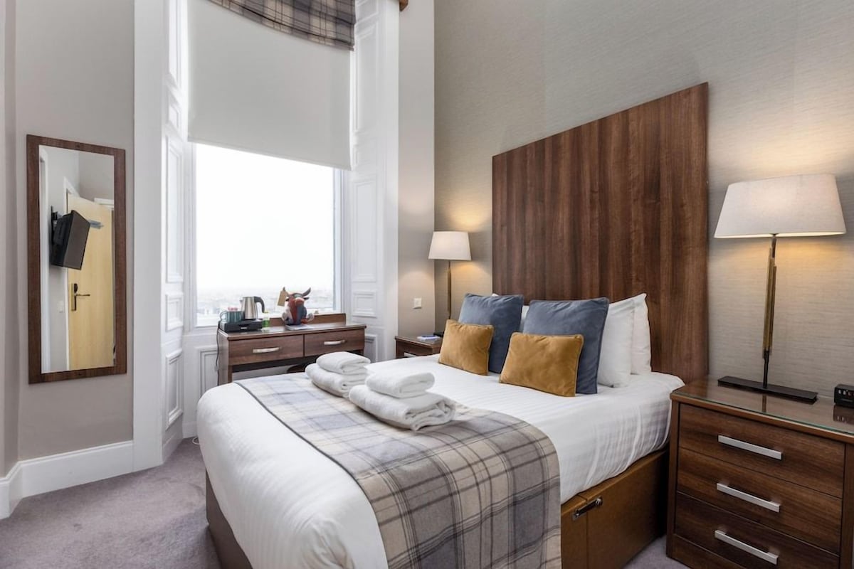 A hotel room with a large bed, bedside tables, a mirror, a wardrobe, and a window with curtains.
