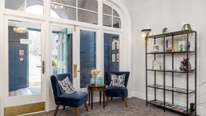 A room with two blue armchairs, a small round table, a bookshelf, and a large arched window. - 28 York Place (Edinburgh)