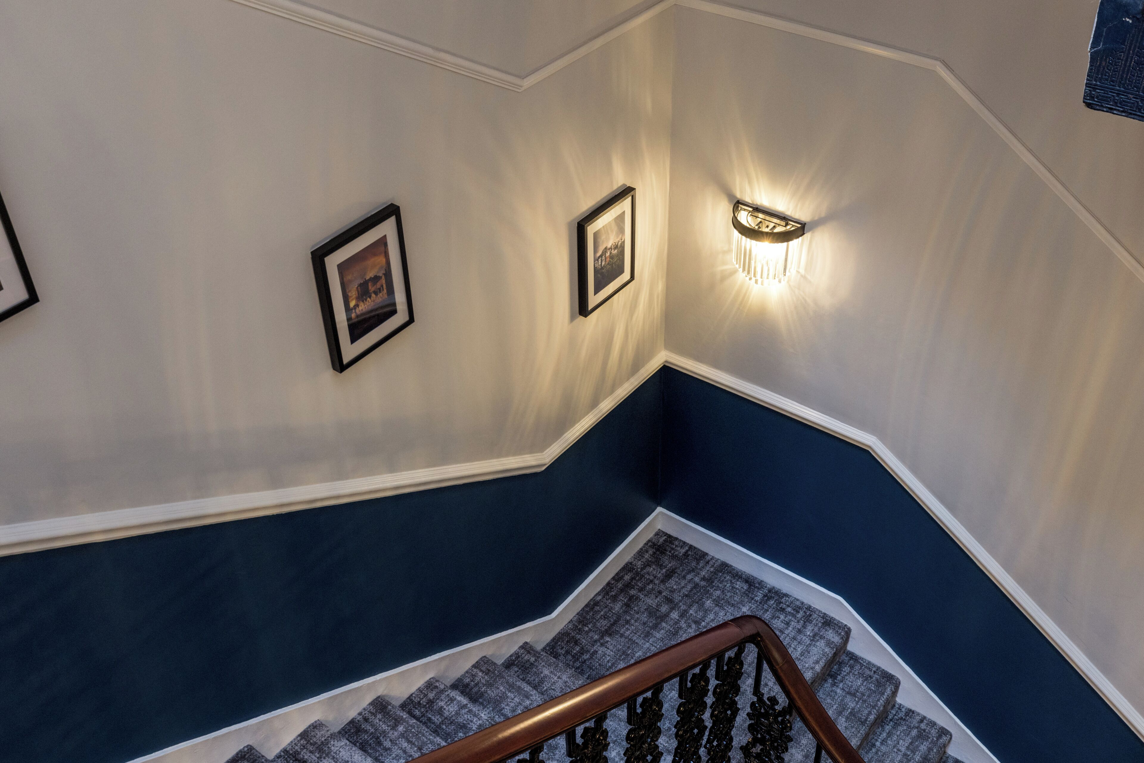 Eine Treppe mit einer Holzhandläufe, einer blauen und weißen Wand sowie gerahmten Bildern.