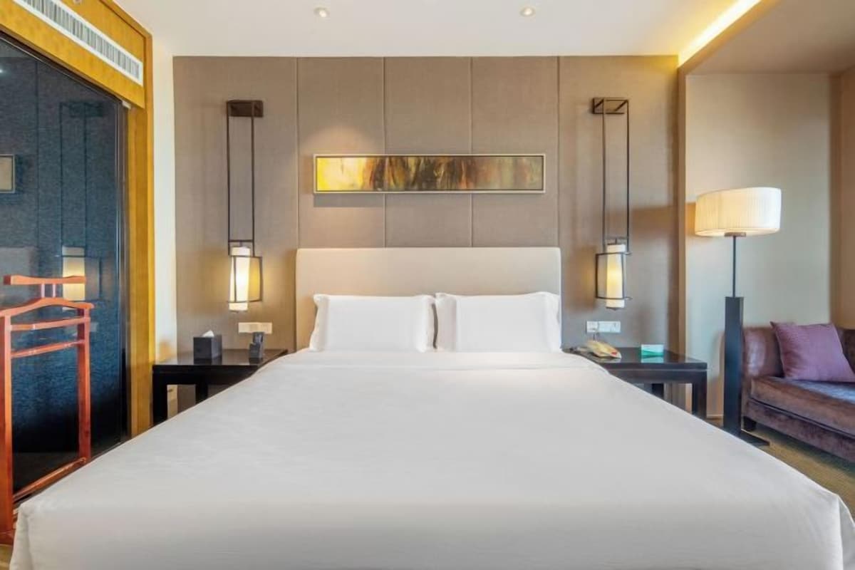 A hotel room with a large bed, two bedside tables, a nightstand, a sofa, and a painting on the wall.