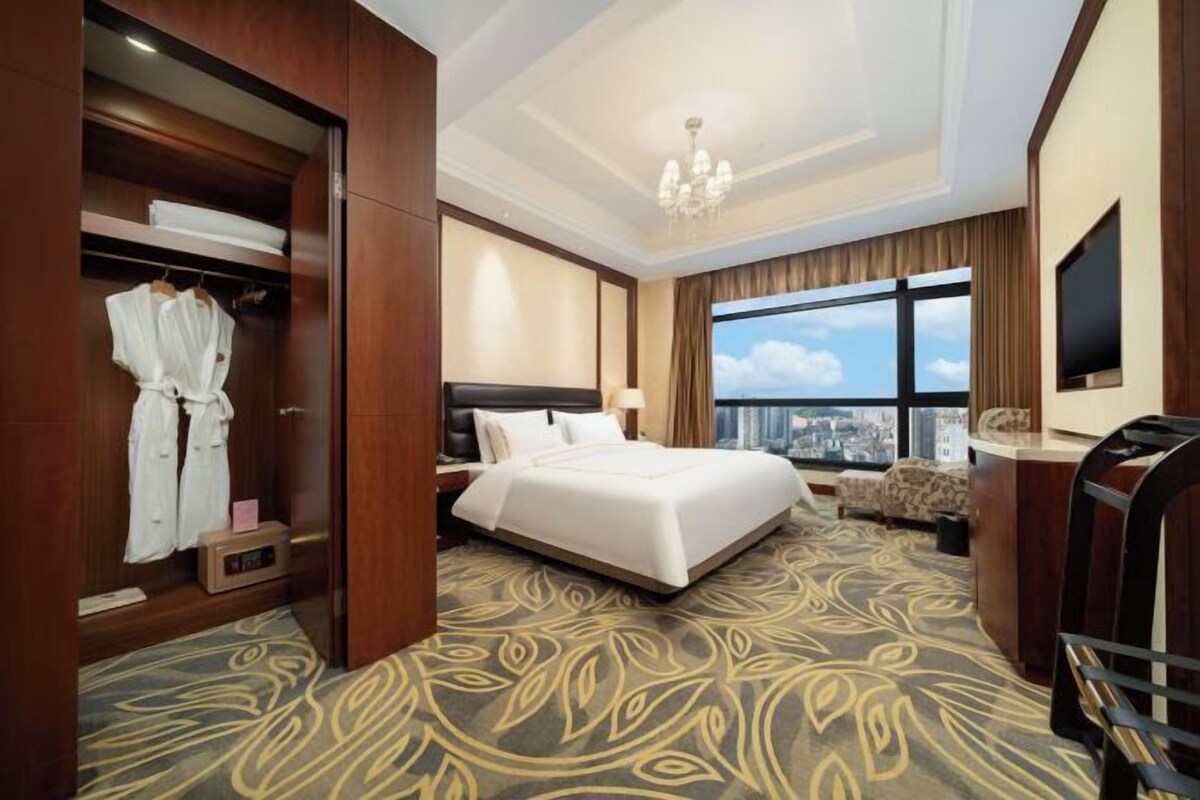 A hotel room with a large bed, a seating area, a wardrobe, and a television.