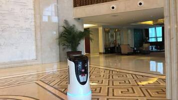 Een robot in een hal met een patroon vloer, een kamerplant en een zithoek op de achtergrond.