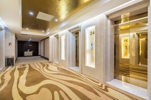 A hotel corridor with a patterned carpet, reception area, and elevators. - Star International Hotel (Suqian)