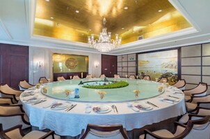 Una mesa redonda de comedor con mantel blanco, rodeada de sillas, en una habitación con una araña y un cuadro grande en la pared.