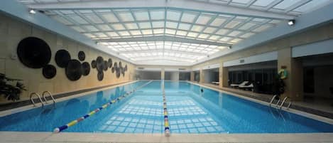 An indoor swimming pool with a glass ceiling, surrounded by lounge areas and a wall with circular decorations.